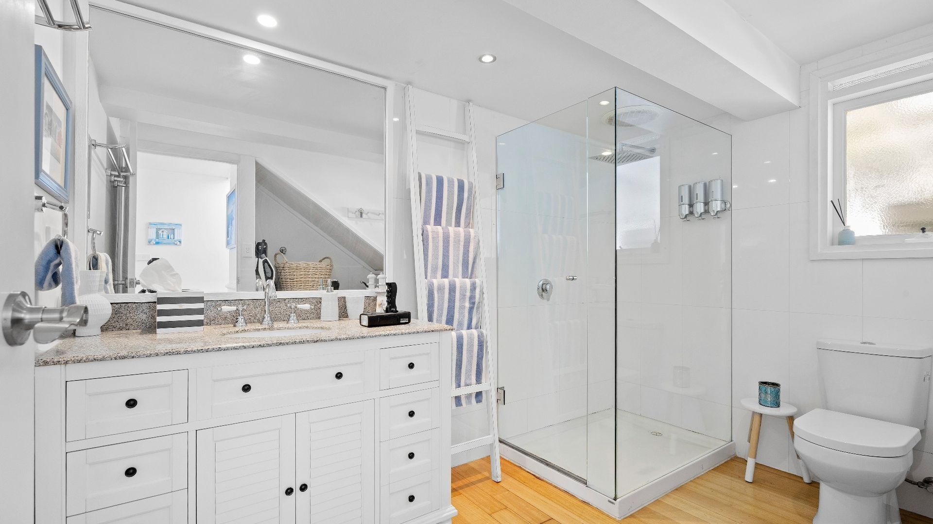 Une salle de bain moderne avec une douche à parois de verre, un lavabo blanc agrémenté d’une serviette à rayures et des toilettes.