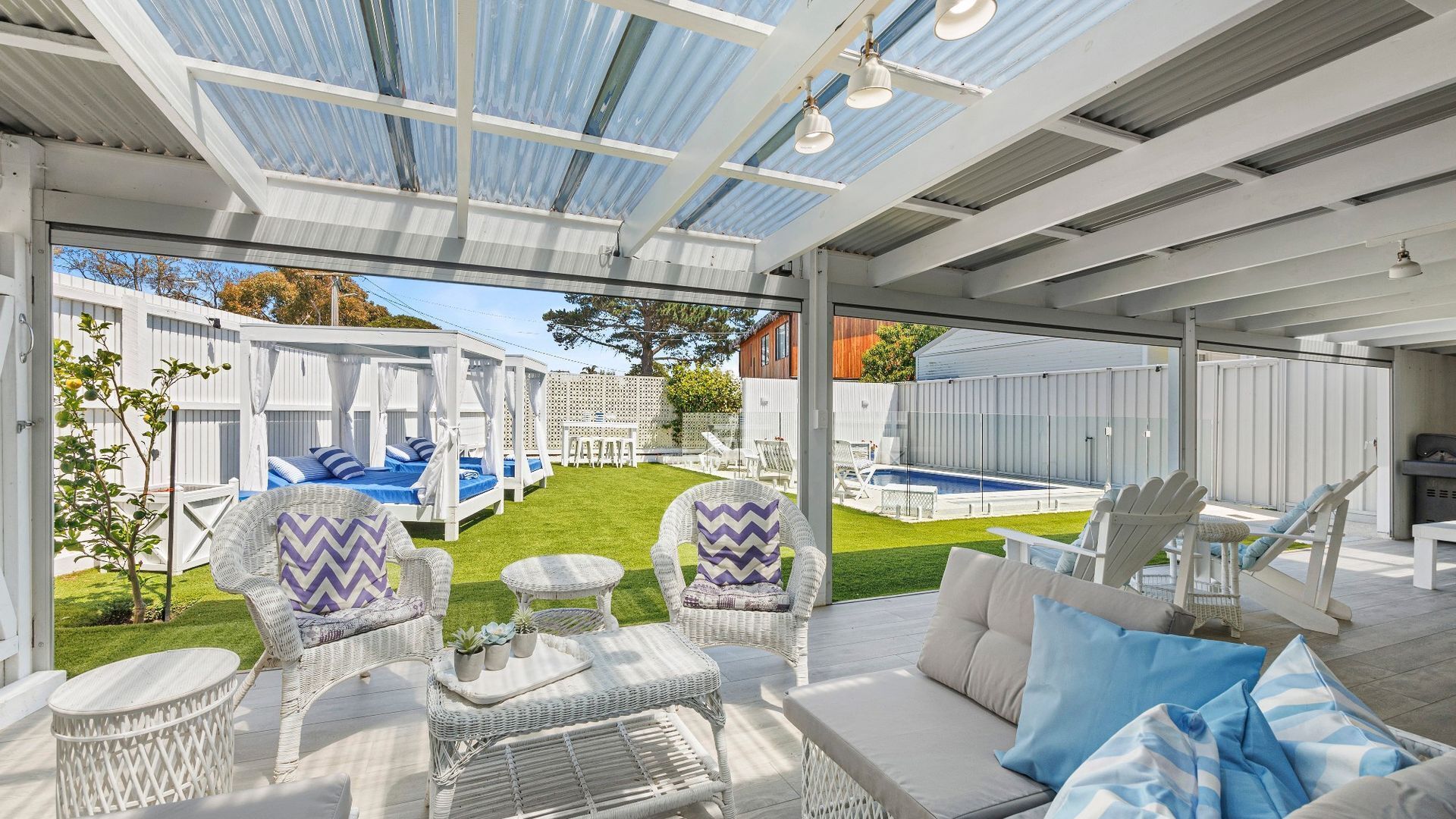 A covered outdoor area with white wicker furniture, a pool, and a well-maintained lawn.