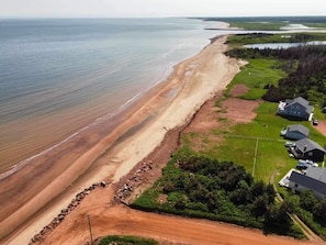 An aerial view of a coastal area with a sandy beach, a grassy field, and a few buildings. - Beach Haven - 17 Rocky Lane (Mount Stewart)