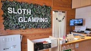 A reception desk with a 'SLOTH GLAMPING' sign, a computer monitor, and various office supplies.