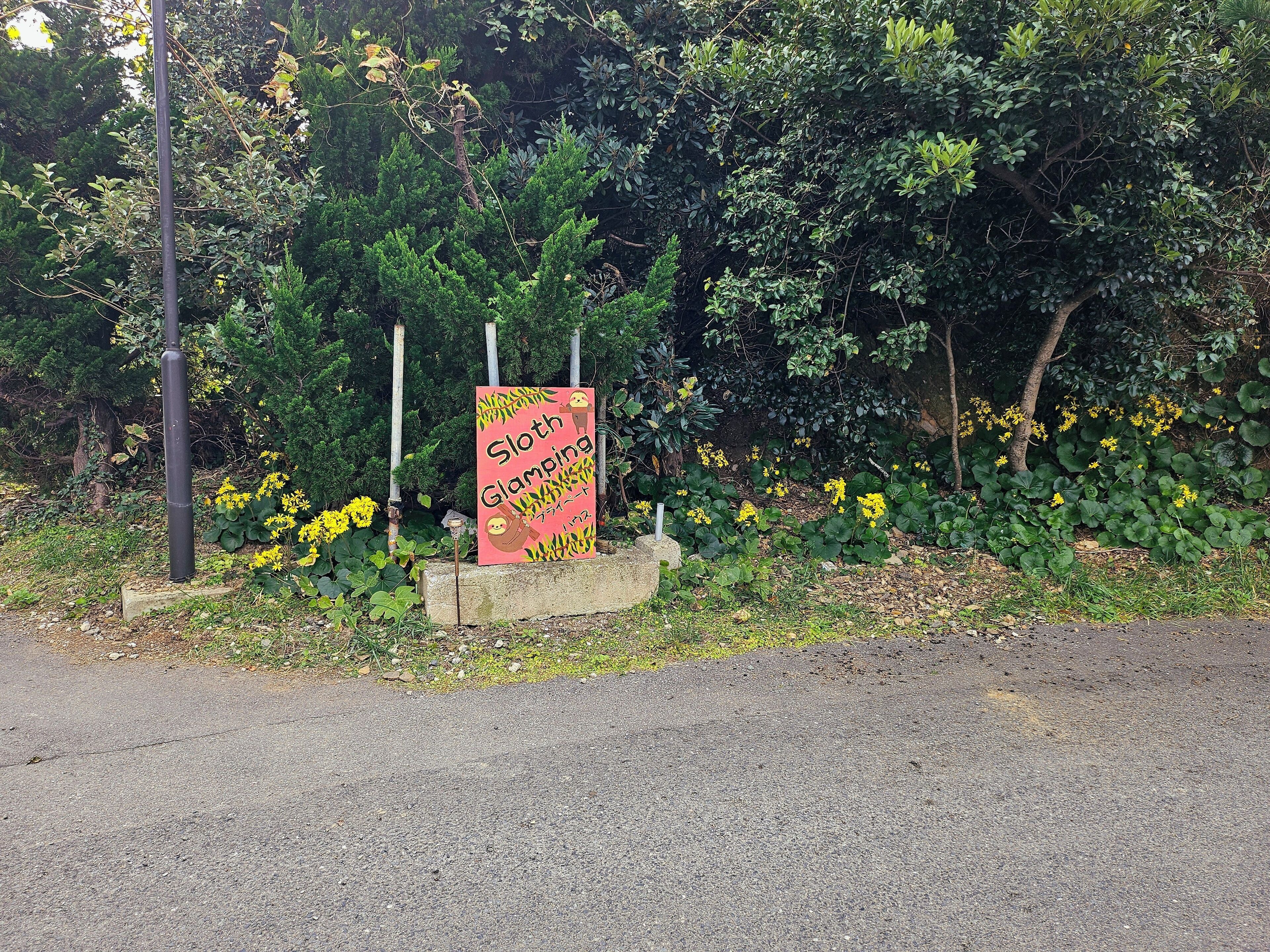 A sign with a sloth and the text "Sloth Glamping" in a garden setting.
