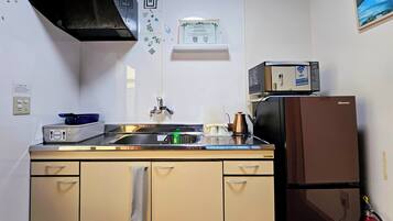 A compact kitchen with a sink, a stove, a refrigerator, and a microwave. There is a towel hanging on the cabinet door, and a fire extinguisher mounted on the wall.