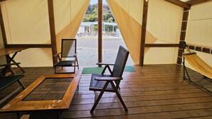 A tented area with wooden flooring, two chairs, a table, and a hammock.