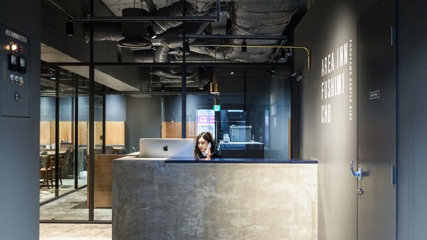A reception desk with a laptop, a person behind it, and a sign reading "AREA INN FUSHIMI CHO". - Area Inn Fushimicho Fukuyama Castle Side 2-8 - Hostel (Fukuyama)