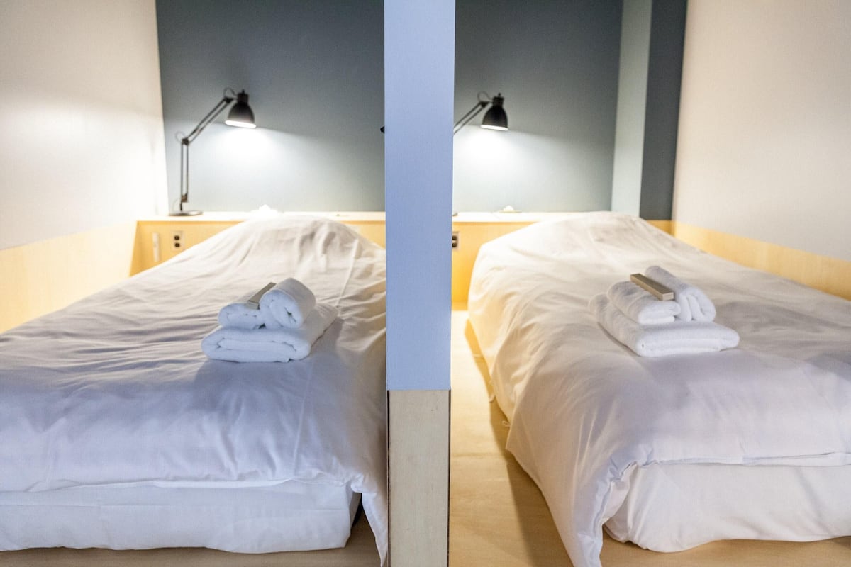 Two identical twin beds with white linens and folded towels, each with a bedside lamp.