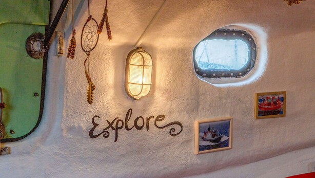 Un mur sur lequel est écrit le mot « Explore » en lettres cursives, une petite fenêtre et un tableau représentant un bateau.