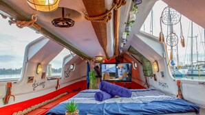 Un intérieur chaleureux d’un bateau, avec un lit, un téléviseur et une petite table agrémentée d’une plante.