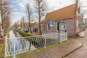 Un bâtiment situé au bord d’un canal, avec un toit recouvert de tuiles rouges, une clôture en métal blanche et un panneau de signalisation bleu.