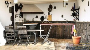 A rustic outdoor kitchen with stone flooring, wooden furniture, and hanging lanterns. - Villa Mareta by Interhome (Tinajo)