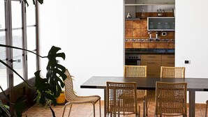 A dining area with a dark table and wicker chairs, a large potted plant, and a kitchen visible through an open door. - Villa Mareta by Interhome (Tinajo)