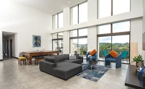 Uma sala de estar ampla com um sofá grande, uma mesa de jantar e uma varanda com vista.