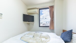 Une chambre d’hôtel avec un lit, un téléviseur fixé au mur et une fenêtre avec un rideau.