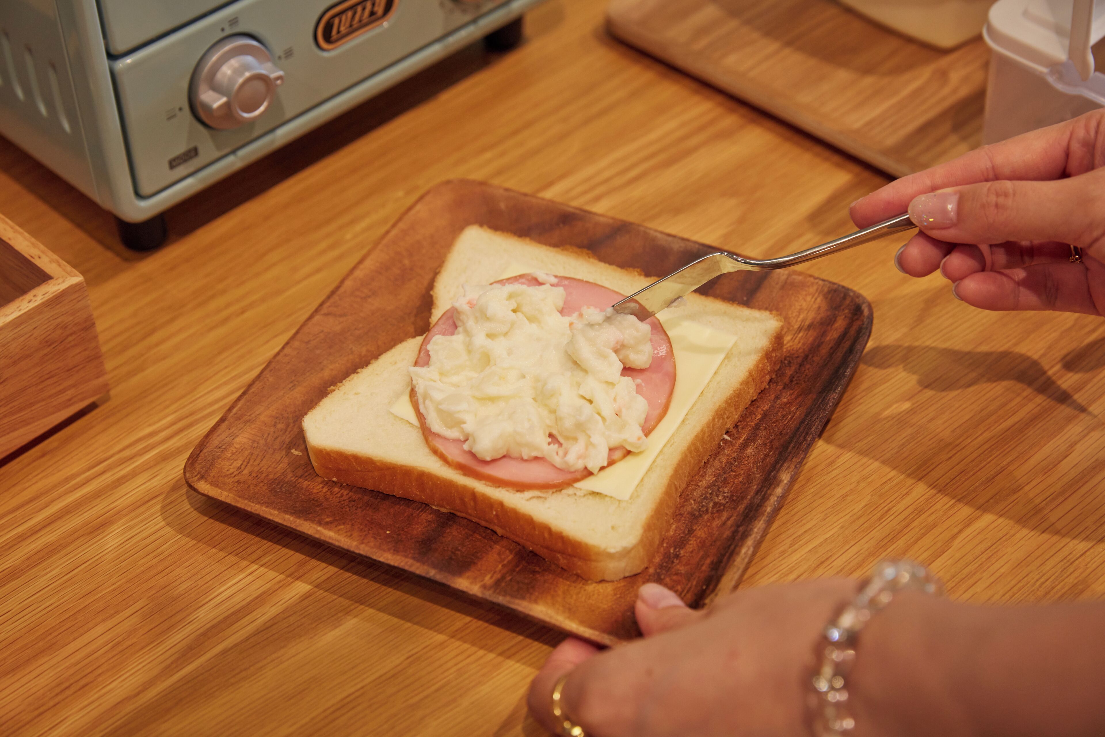 A slice of bread with cheese and ham on a wooden cutting board.