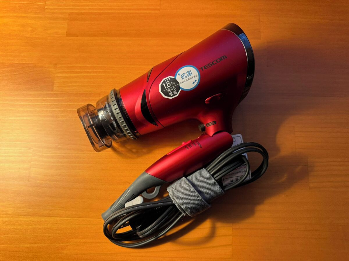 A red hairdryer with a cord and a protective cover on a wooden surface.