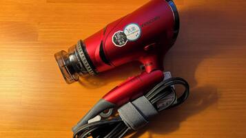 A red hairdryer with a cord and a protective cover on a wooden surface.