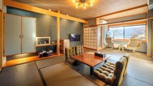 Una habitación tradicional japonesa con suelo de tatami, una mesa de madera baja, asientos acolchados y un televisor.