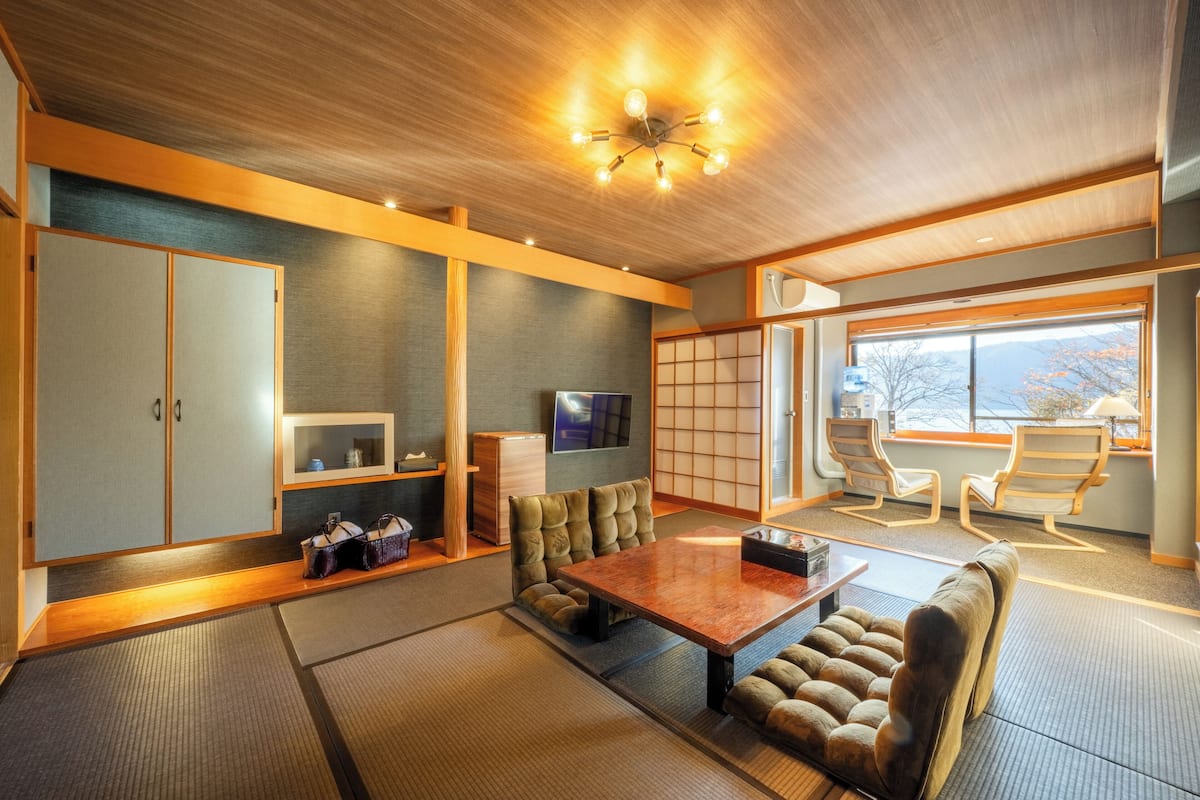 Habitació d'estil japonès tradicional amb fons de tatami, taula de fusta baixa, seients amb coixins i un televisor.