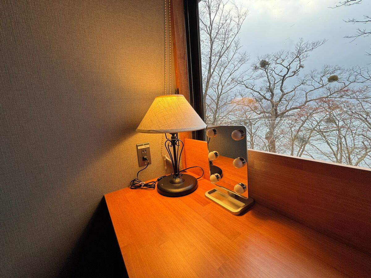 A wooden bedside table with a lamp, a mirror, and a power outlet.