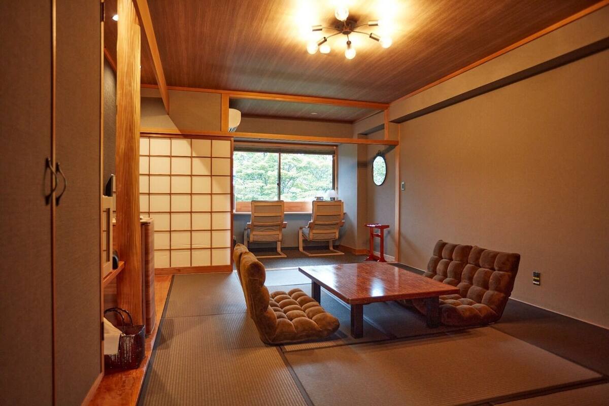 Habitació japonesa tradicional amb fusteria de tatami, una taula baixa, seients amb coixins i un panell shoji.