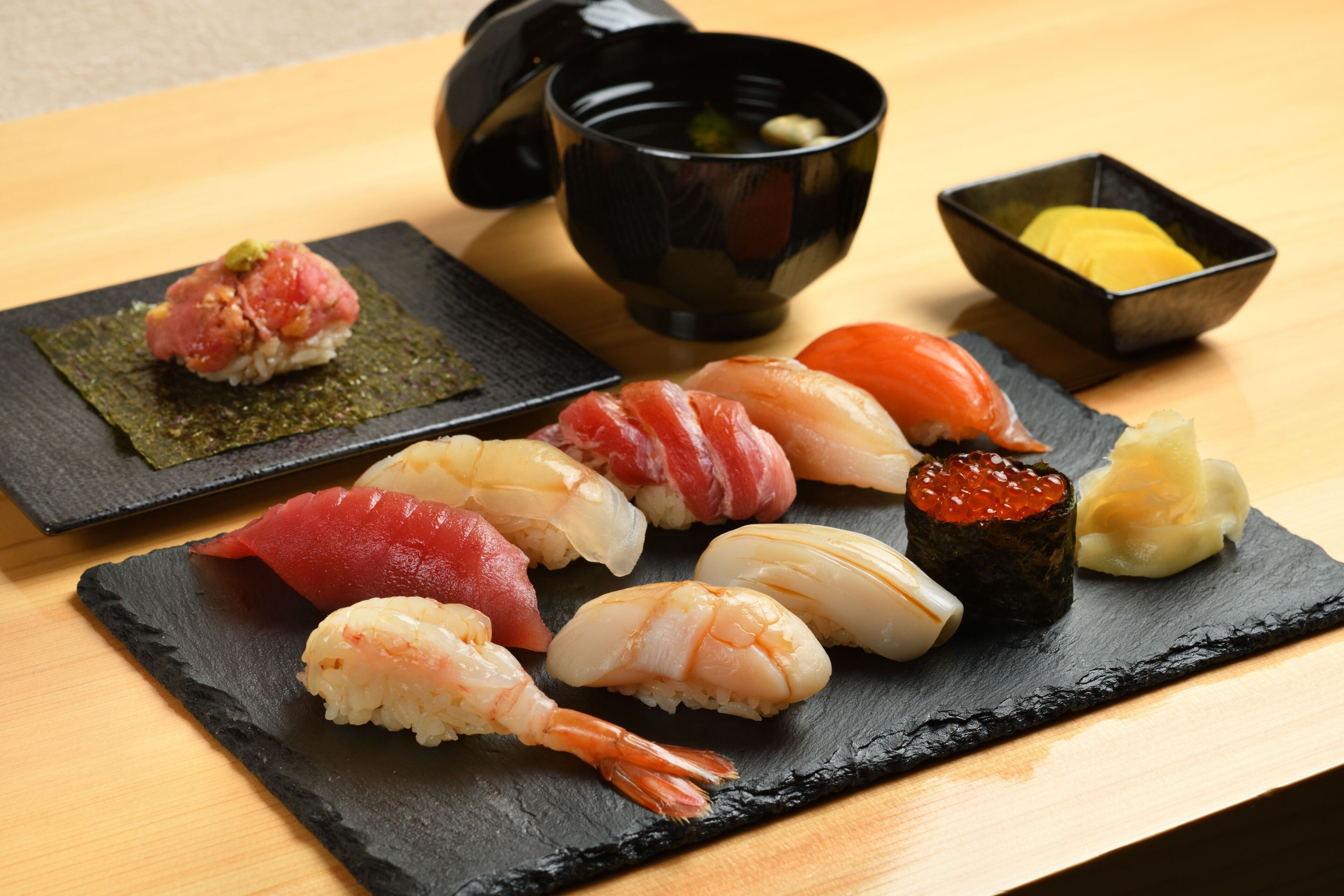 A variety of sushi on a slate plate with a black bowl and a small dish of wasabi.