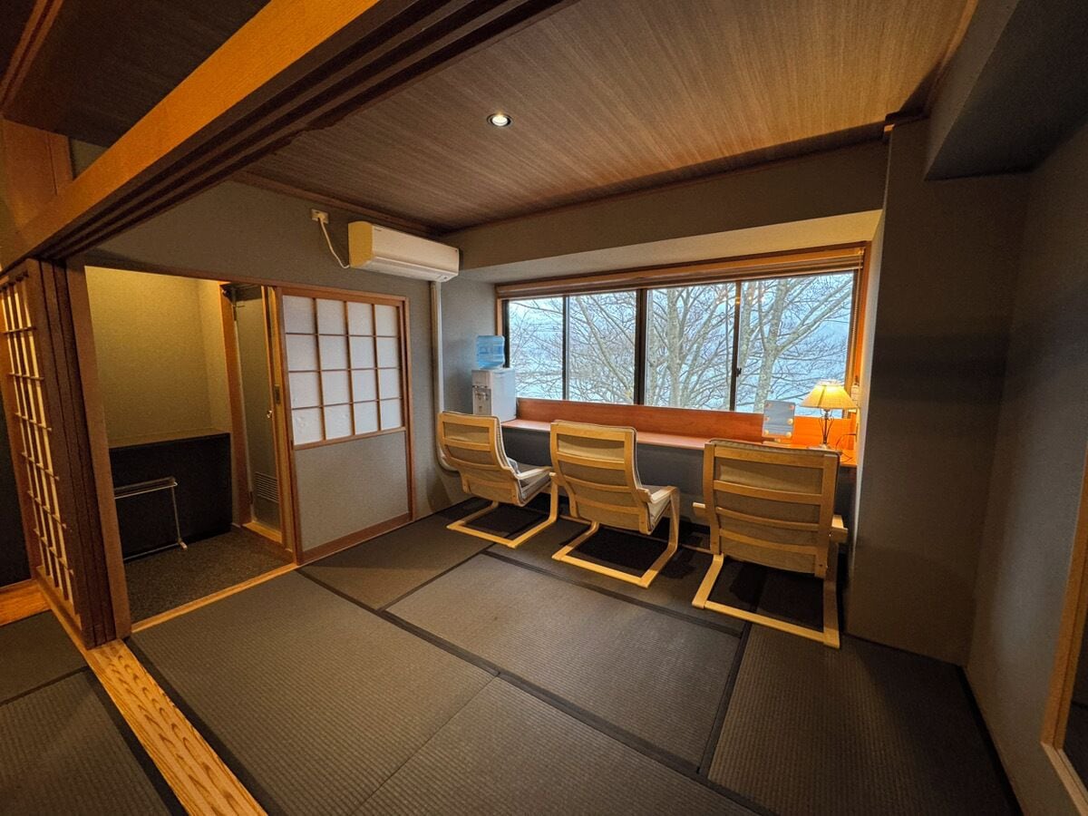 A traditional Japanese room with tatami flooring, a shoji screen, and a view of trees through the window.