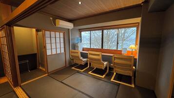 A traditional Japanese room with tatami flooring, a shoji screen, and a view of trees through the window.