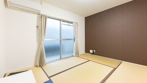 Una habitación con suelo de tatami, puerta corredera de vidrio y aire acondicionado instalado en la pared.