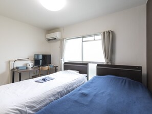 Una habitación de hotel con dos camas, un escritorio con televisor, un hervidor y una ventana con cortinas.