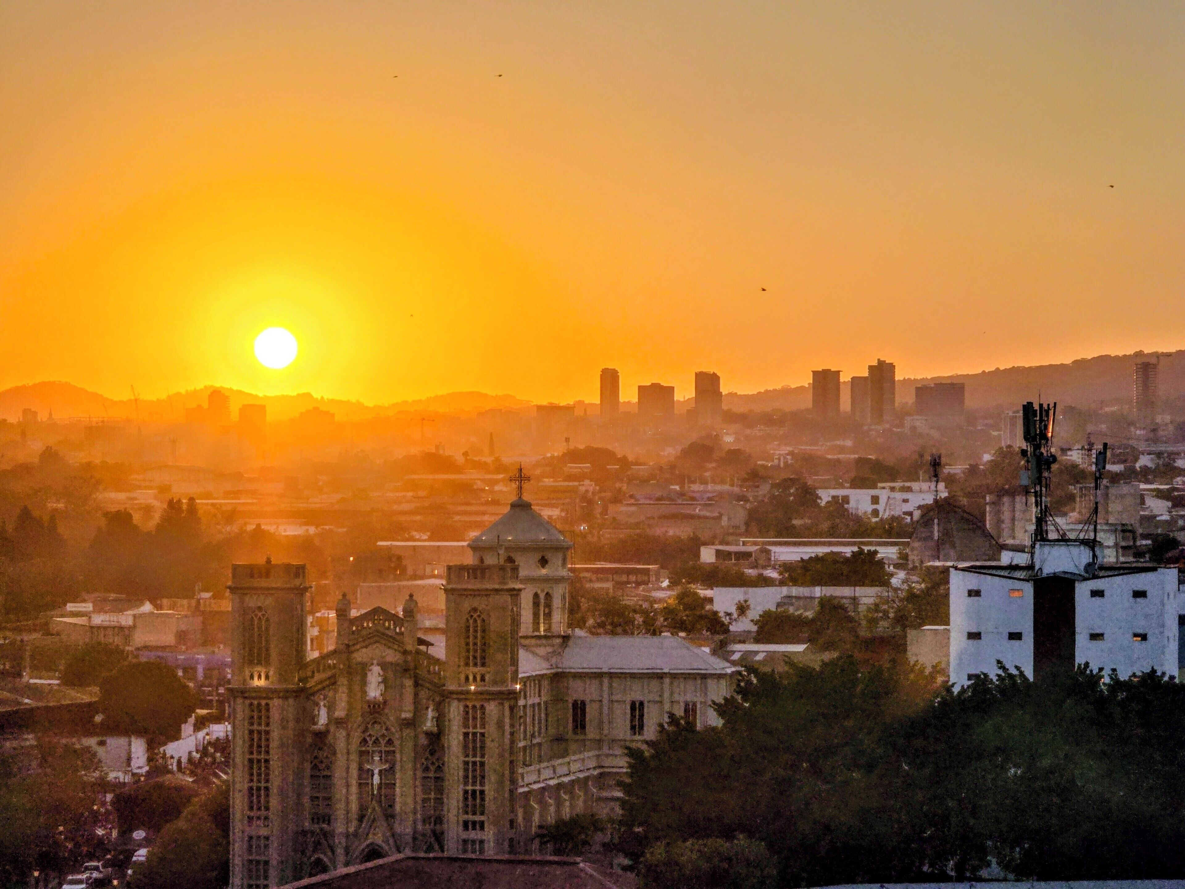 Eine Stadtansicht mit einem markanten Kirchturm und modernen Gebäuden bei Sonnenuntergang.