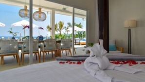 Una camera d'albergo con un letto, un'area pranzo con sedie e ombrelloni, e vista sull'oceano.