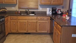 A kitchen with wooden cabinets, a granite countertop, a sink, and a 'WINE' sign above the cabinets. - Winding Meadows Home Away from Home (Bolingbrook)