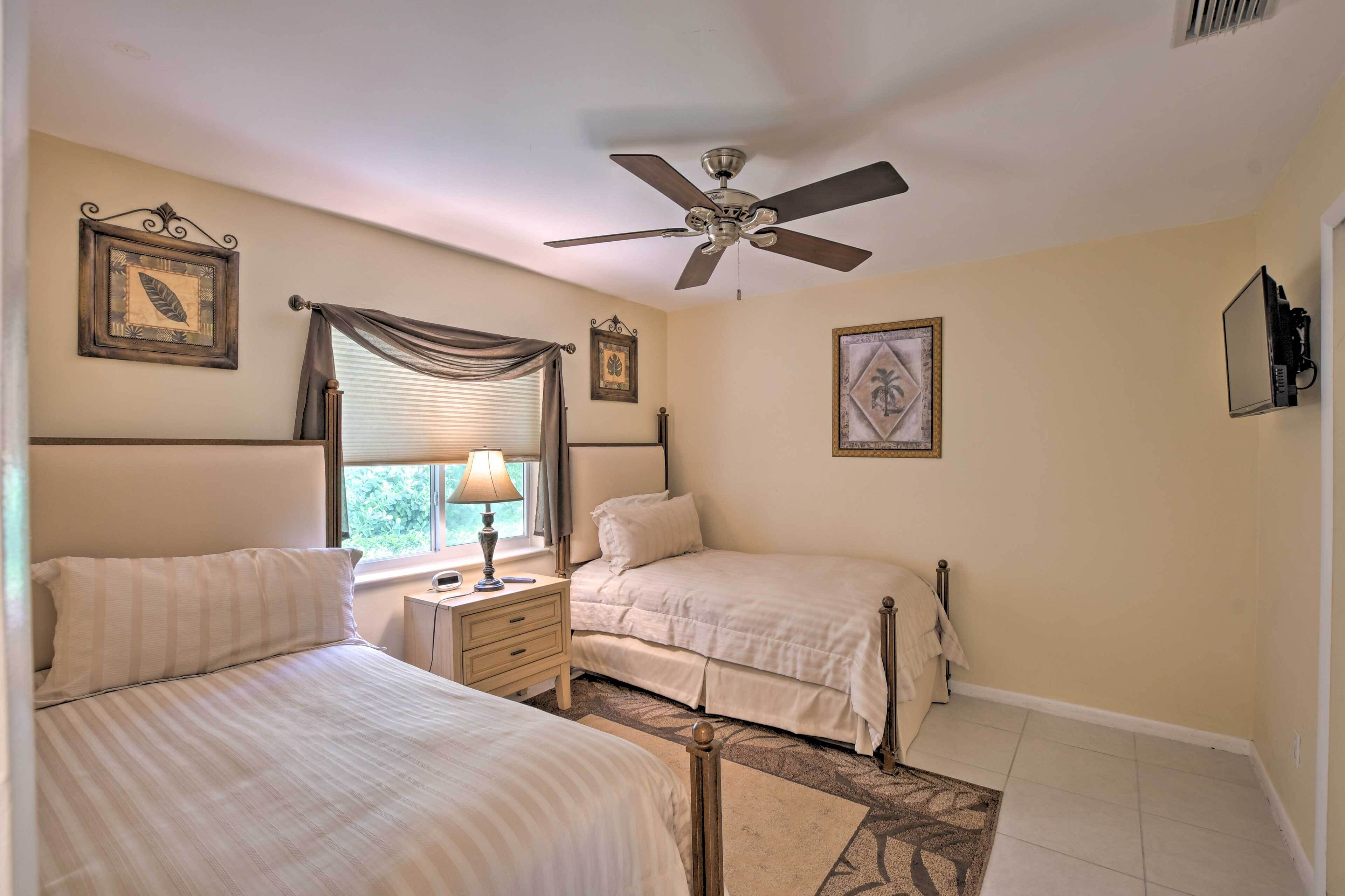 A bedroom with two beds, a ceiling fan, a nightstand, a lamp, and framed pictures on the walls.