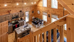 A cabin with a wooden interior, a kitchen with modern appliances, a dining area with a table and chairs, and a staircase leading to a loft bedroom.