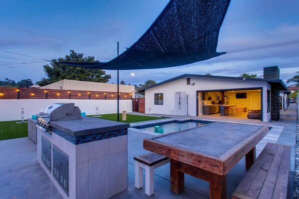 An outdoor patio with a grill, a pool table, and a covered seating area.