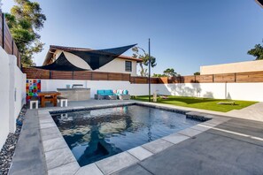 A modern outdoor pool area with a wooden deck, a seating area with a sofa and chairs, and a well-maintained lawn.