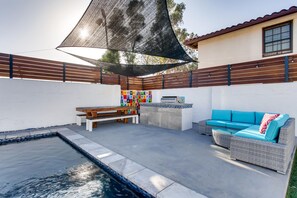 A backyard with a swimming pool, a barbecue area, a sofa, and a wooden bench.