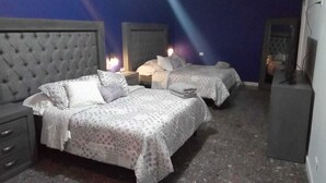 Een hotelkamer met twee bedden, een grijs hoofdeinde, een nachtkastje met een lamp en een klein kastje.