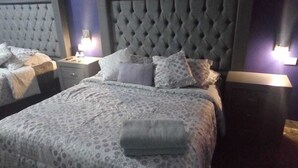 Een slaapkamer met een gestoffeerd hoofdeinde, een bed met een patroon en twee bedlampen.