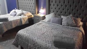 Een hotelkamer met twee bedden, elk met een gestoffeerd hoofdeinde, een nachtkastje en een lamp.