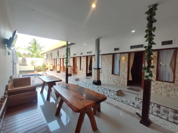 A spacious outdoor area with wooden benches and tables, stone pillars, and a tiled floor.