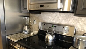 Una cocina con un microondas de acero inoxidable, una cocina vitrocerámica negra, un hervidor y una licuadora en la encimera.