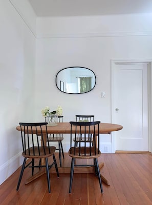 Un comedor con una mesa de madera y cuatro sillas, un espejo en la pared y una puerta blanca.