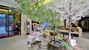 Un espace intérieur moderne, agrémenté d’arbres artificiels, d’un comptoir d’accueil et de coins salon.