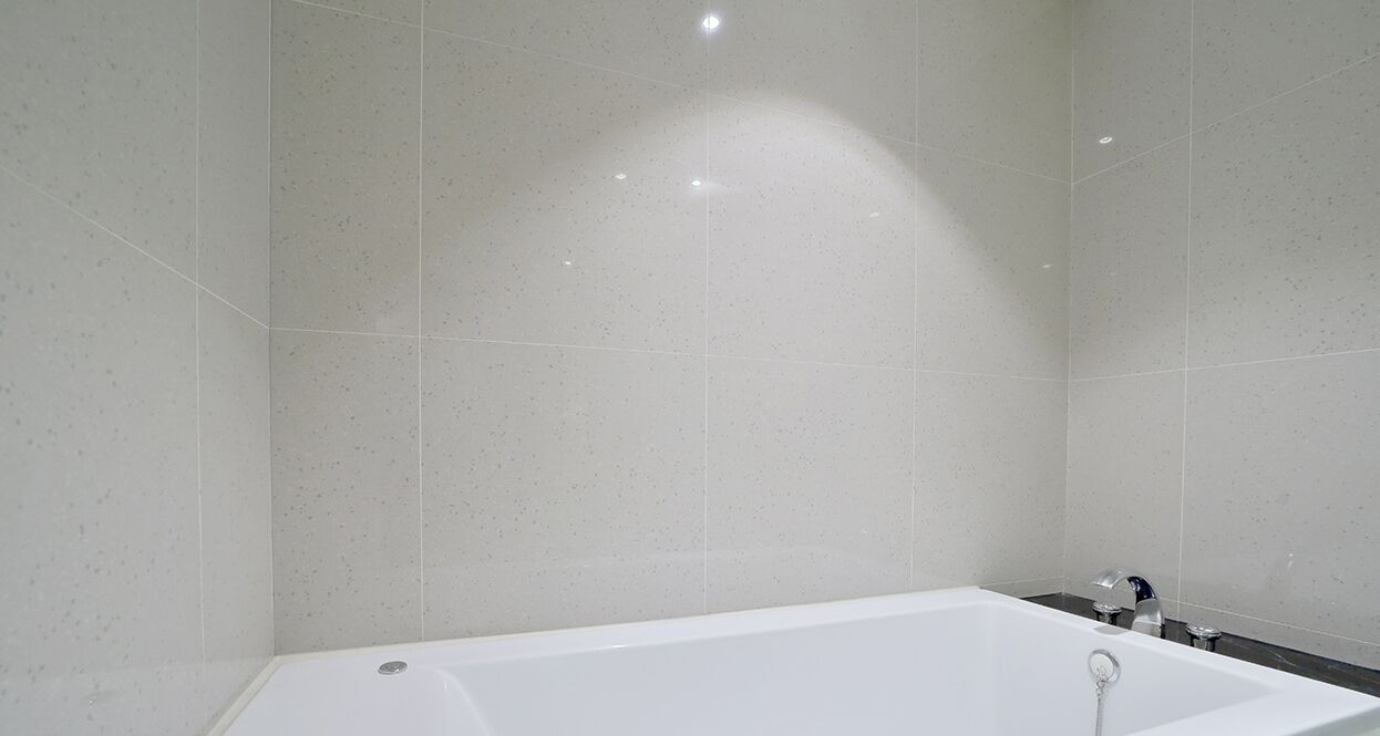 Un baño moderno con una bañera blanca, paredes cubiertas de azulejos y una única lámpara.