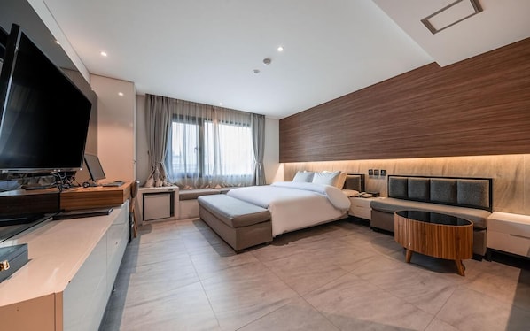 A modern hotel room with a bed, bedside tables, a TV, and a seating area.