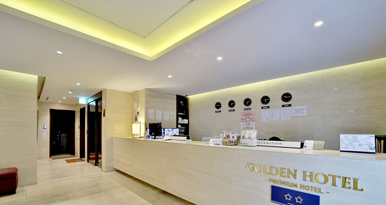 A reception desk at the Golden Hotel with a modern design, a clock, and informational posters on the wall.