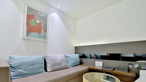 Une chambre d’hôtel moderne avec un canapé, une table de chevet avec une lampe et un tableau au mur.