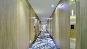 Un long couloir aux murs lambrés, un tapis à motifs et un ascenseur situé sur la droite.