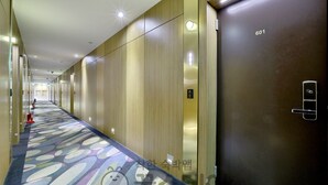 Un couloir d’hôtel avec un tapis à motifs, des murs recouverts de panneaux de bois et un ascenseur portant le numéro 601.