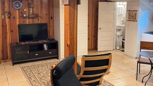 Ein Wohnzimmer mit Fernseher, Holzmöbeln, einem Teppich und einer Tür zum Badezimmer.